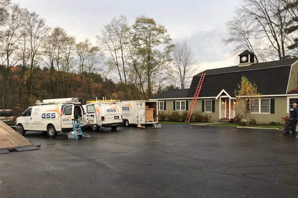Two white dental service vehicles parked outside green dental office building in daytime.