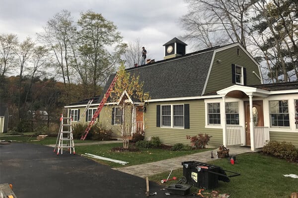A green residential house with white trim under construction or renovation, surrounded by landscaping and equipment.