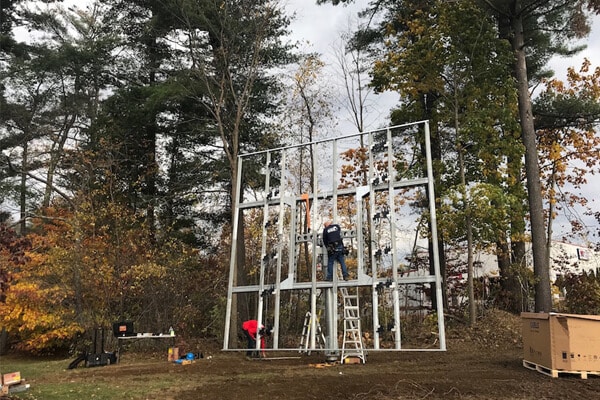 Children climbing on outdoor playground structure in wooded park setting during autumn.