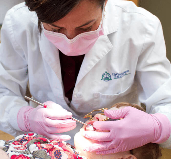 Dental professional in white coat and pink mask examining patient's teeth during dental procedure.