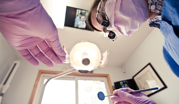 Dental professional in gloves examining patient's teeth using intraoral camera in clinical setting.