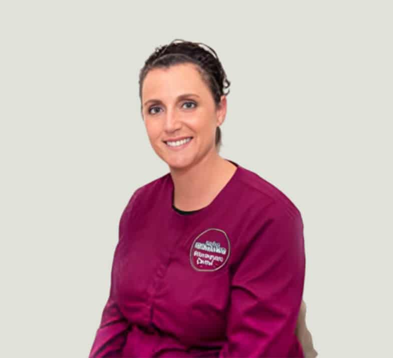 Woman in maroon dental office shirt smiling at camera against neutral background.