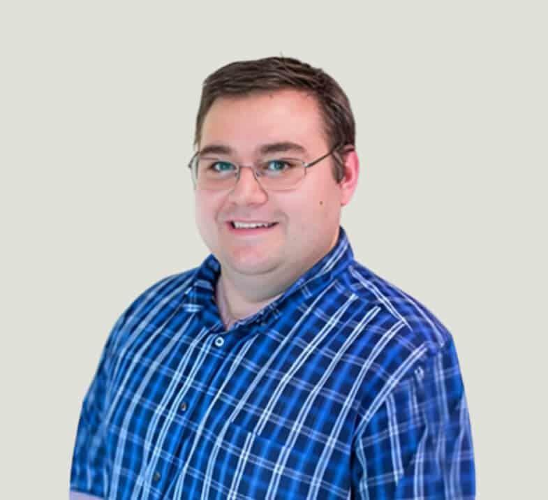 Professional headshot of male dentist wearing blue striped shirt and glasses against neutral background.