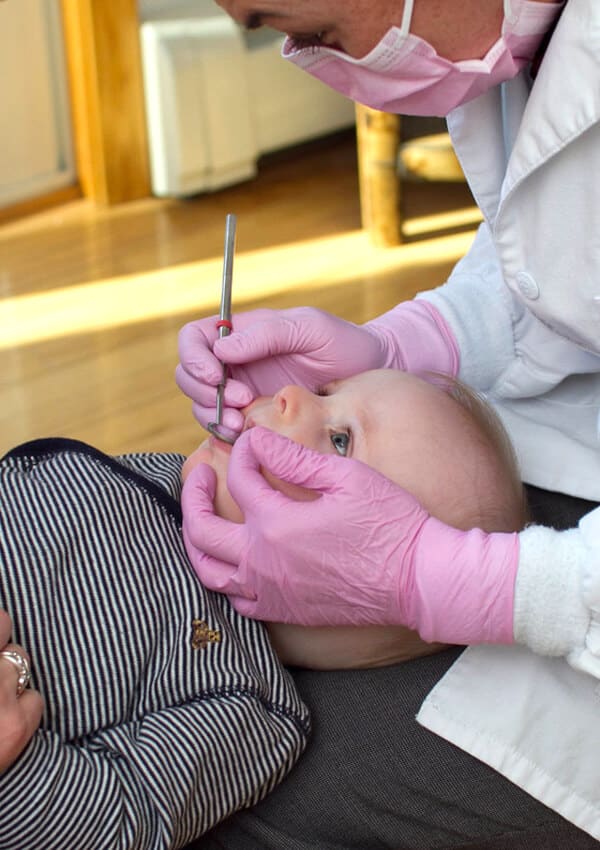 Dentist in pink gloves examines child's teeth during dental checkup appointment.