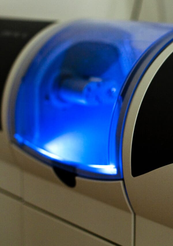 Blue LED dental curing light glowing during dental treatment procedure.