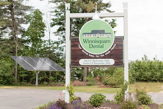 Winnisquam Dental roadside sign with logo displayed in front of landscaped entry and trees.