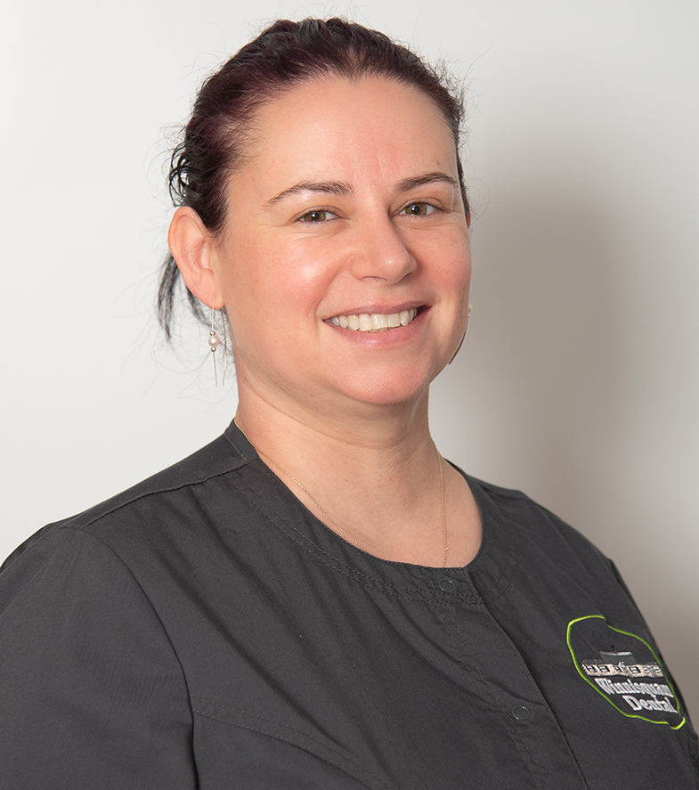 Woman smiling at camera wearing dark dental clinic shirt, professional headshot portrait.