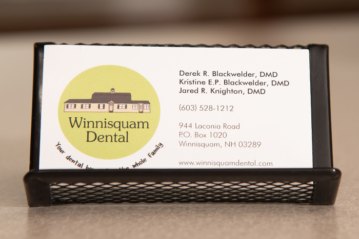 Winnisquam Dental business card displaying logo, dentist names, and contact information on desk.