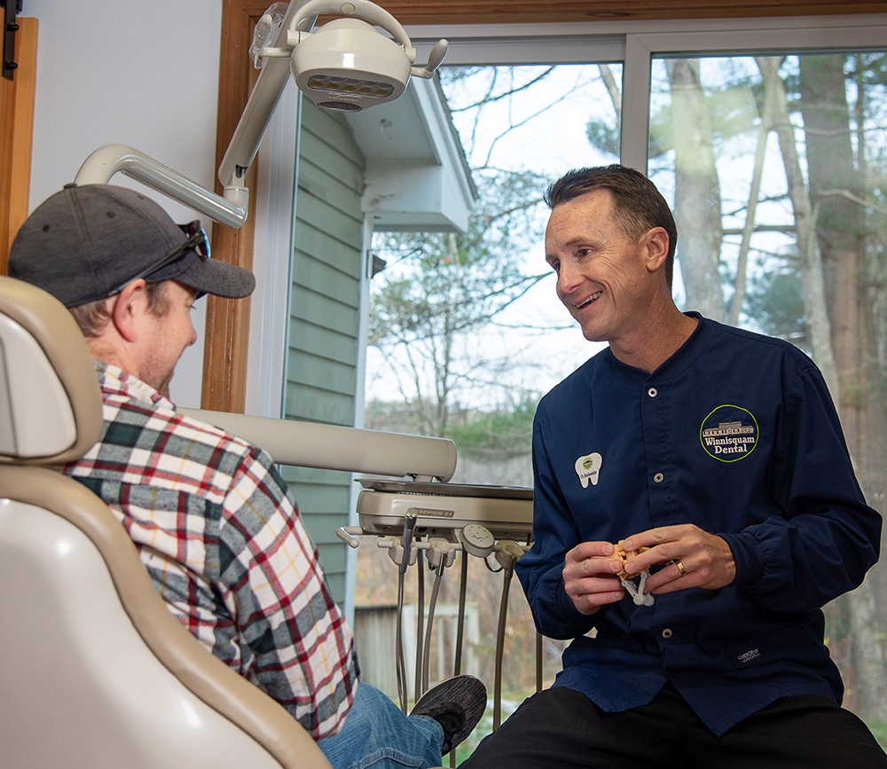 Dentist in navy scrubs consulting with patient in dental office treatment room.