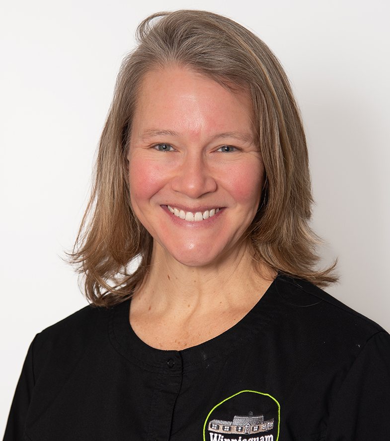 Professional headshot of smiling woman wearing black Winnisquam Dental branded shirt against white background.