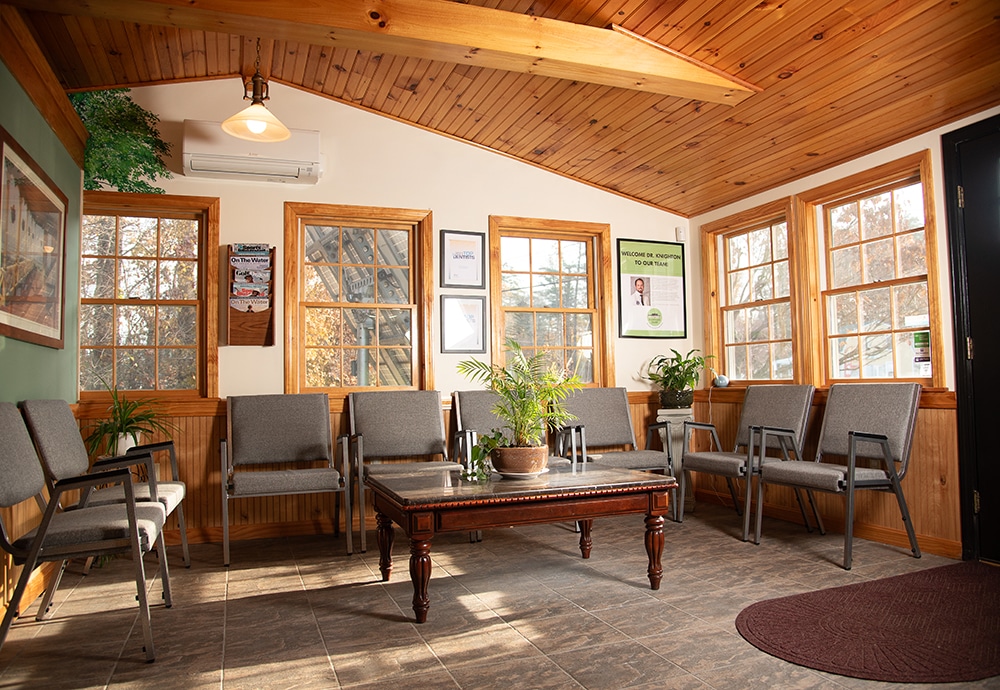 Warm wooden dental waiting room with comfortable seating, framed artwork, and natural light from windows.