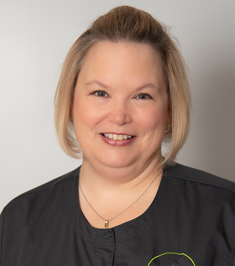 Professional headshot of smiling woman wearing black shirt against neutral background for dental practice.