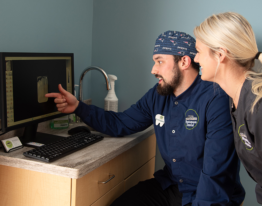 Dental professional demonstrates digital imaging on computer screen to patient in clinical setting.
