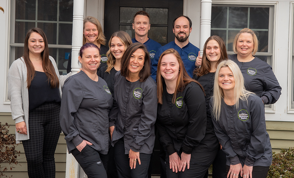 Winnisquam dental team group portrait, professional staff in dark business attire outdoors.