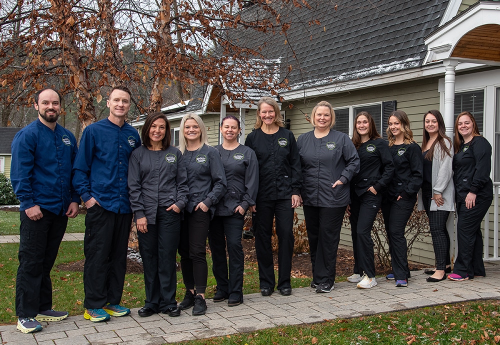 Winnisquam dental team standing together outside brick building in professional attire.