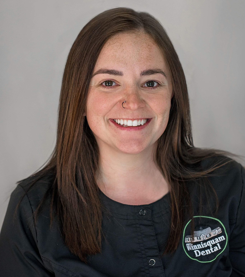 Smiling dental professional in dark scrubs with Winnisquam Dental logo against neutral background.