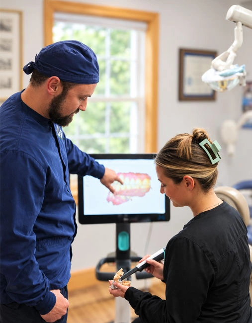 Dentist pointing to a digital dental X-ray on screen while a staff member holds a scanning device in the treatment room