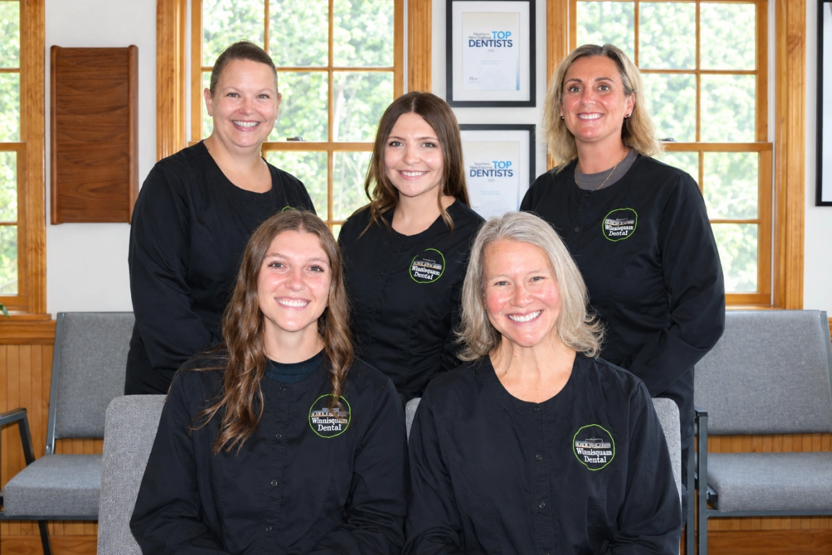Winnisquam Dental hygiene team of five, smiling in matching black scrub jackets indoors