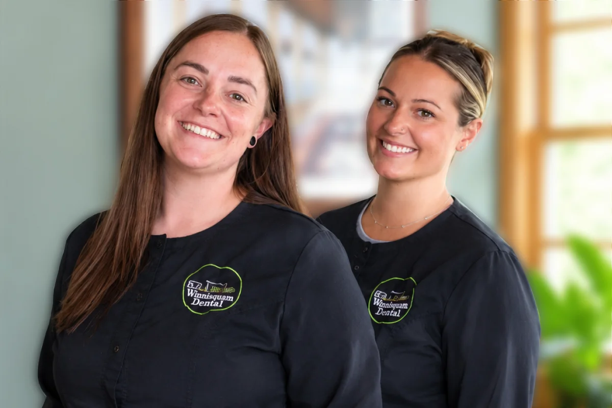 Two smiling Winnisquam Dental staff members in matching black scrub jackets